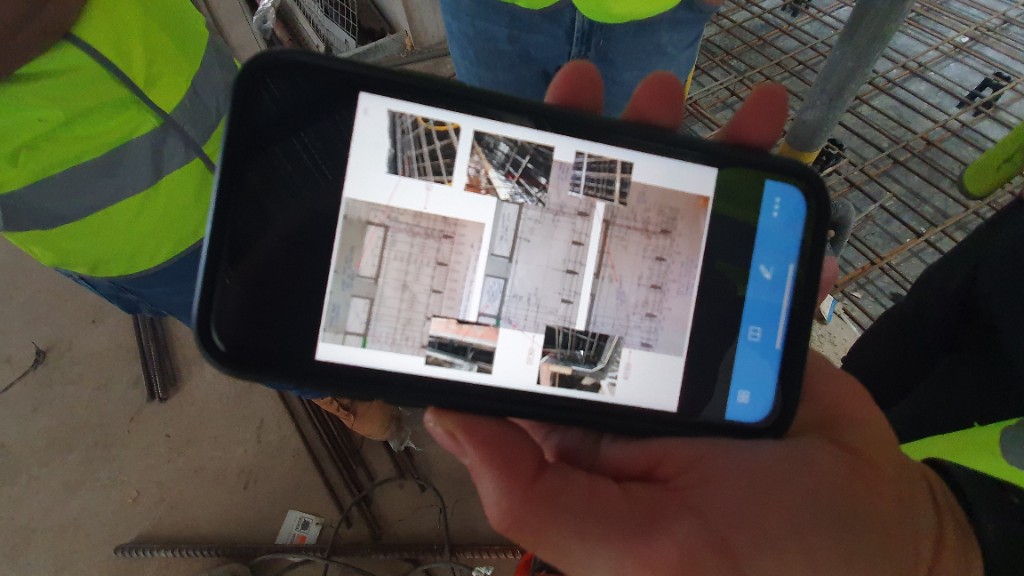 Supervisor viewing construction drawings on a mobile phone with pinned site photos on the plan.