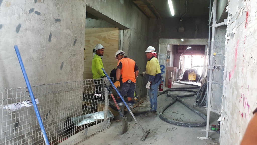 Trades working on an interior floor while site managers conduct inspection rounds.